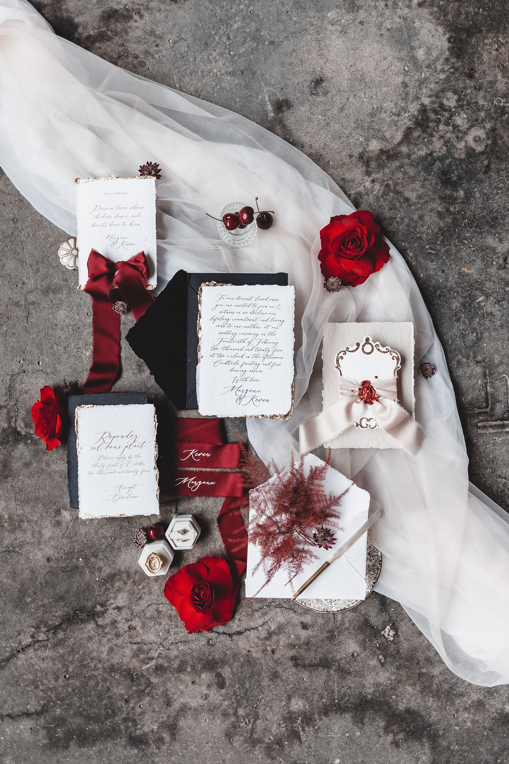 overview shot of wedding stationery, deep red florals and cherries as part of a dark romance wedding
