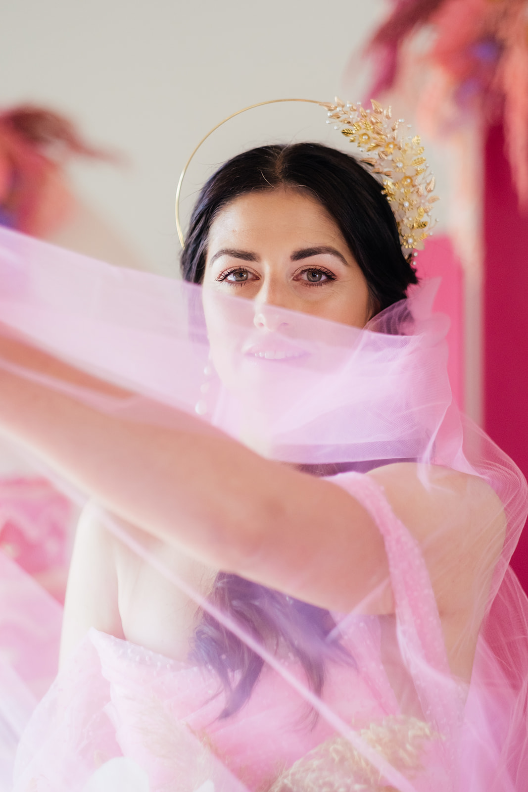 Bride wearing a crown swooshing a pink veil across her face
