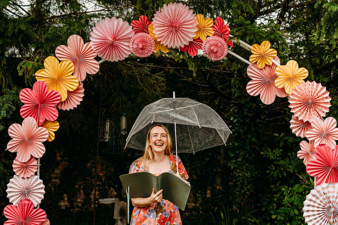 celebrant holding an umbrella under a paper flower arch