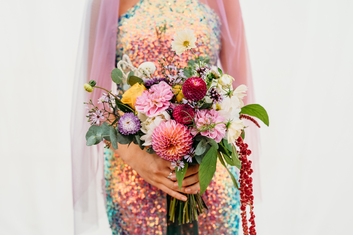 detail shot of colourful wedding bouquet for festival wedding. The brides sequin jumpsuit is visible behind