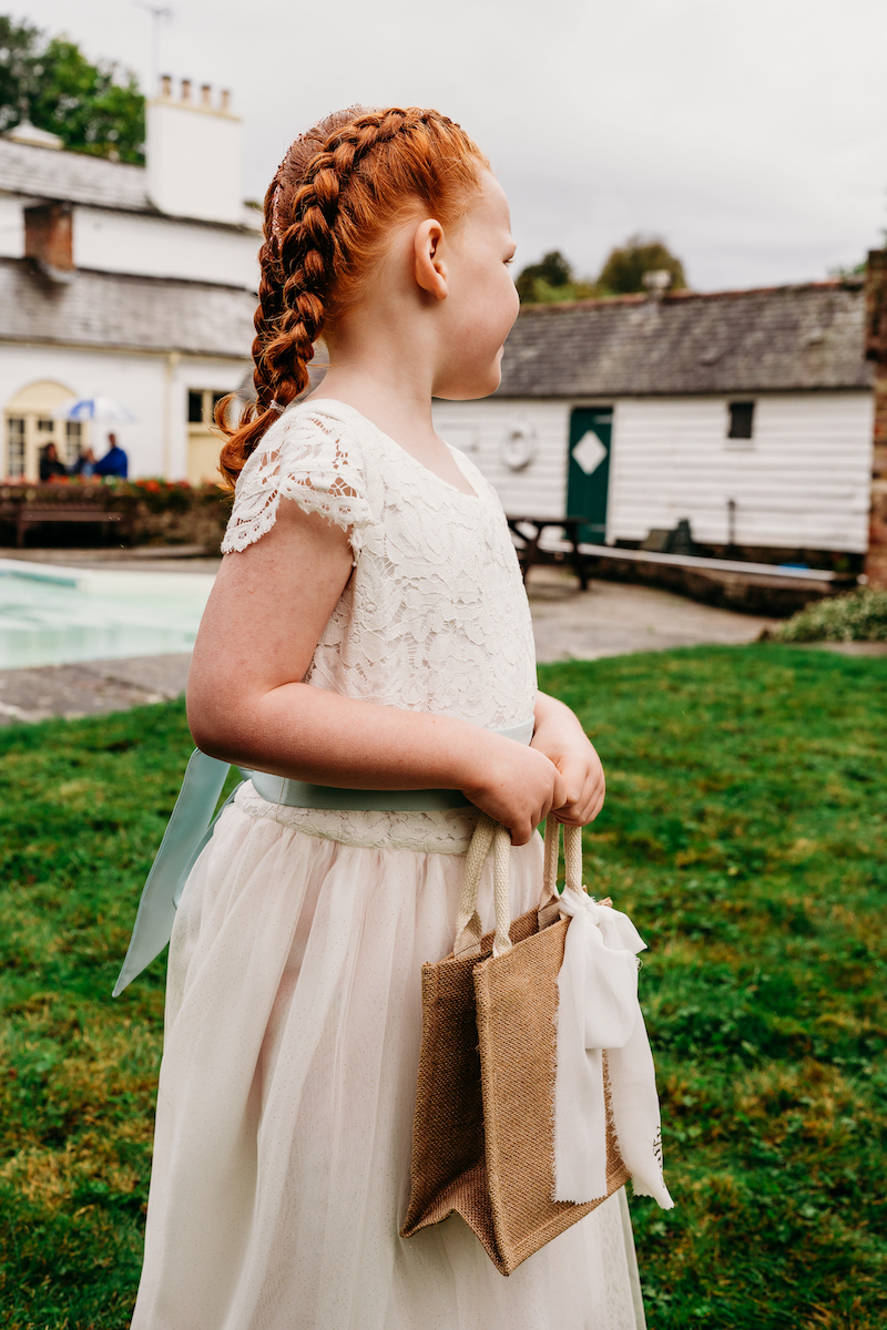 flower girl wearing a lace topped dress holding a confetti bag