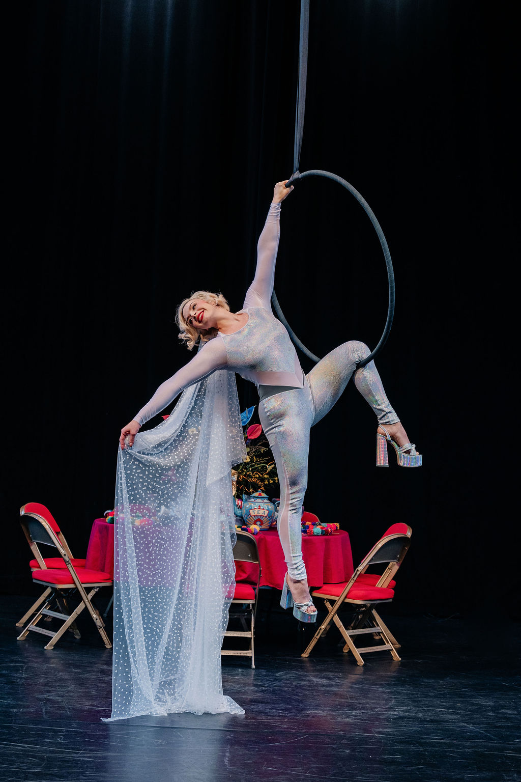 bride in silver jumpsuit suspended from an areal hoop holding out her wedding veil