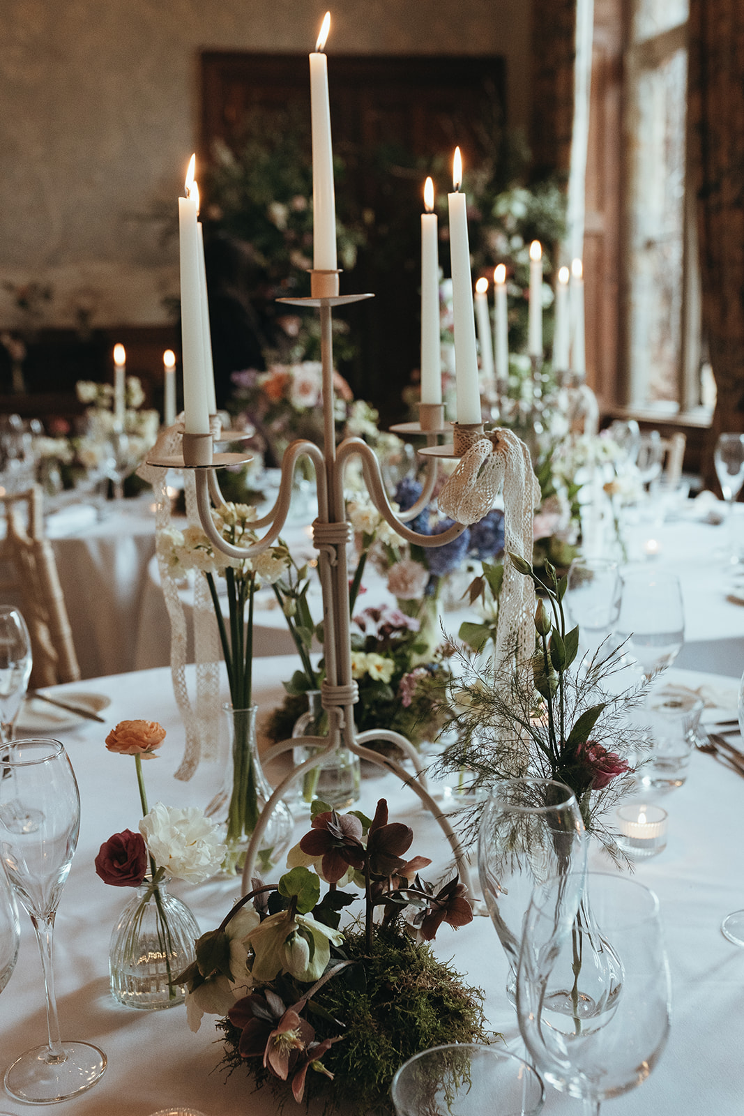 detail shot of lace tied candelabras and moss covered flowers on the wedding breakfast tables for enchanted forest wedding