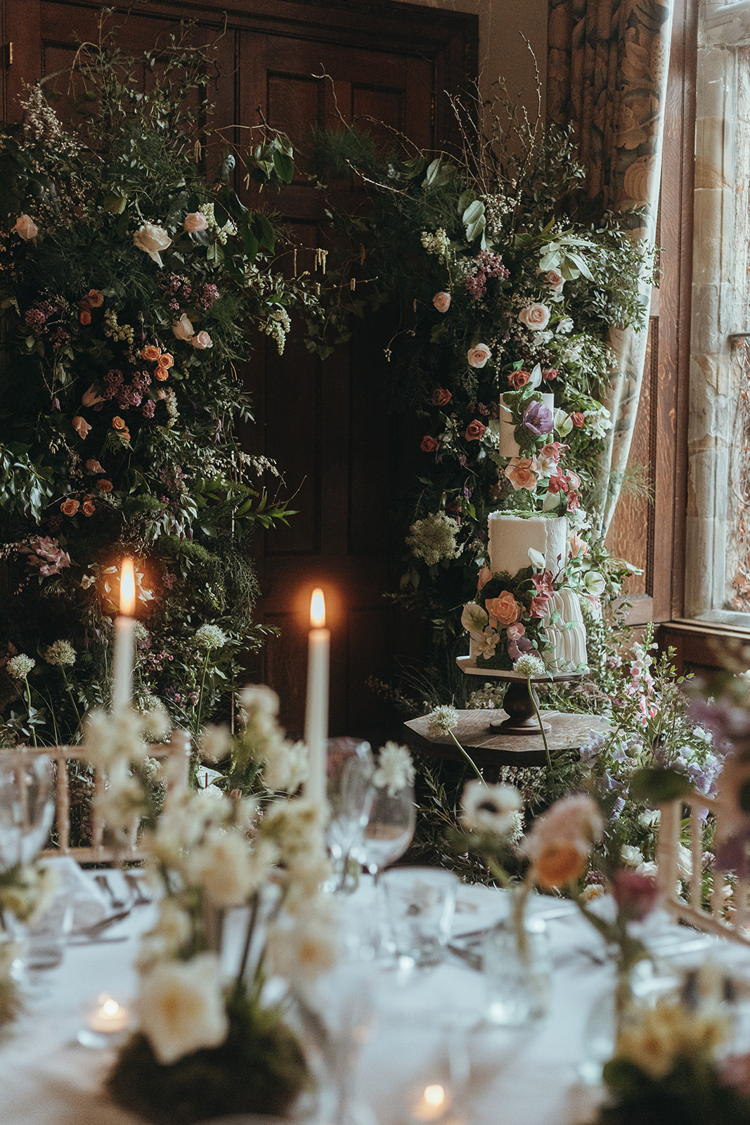 long view through the wedding venue showing wedding cake, statement floral instillation and the wedding breakfast tables