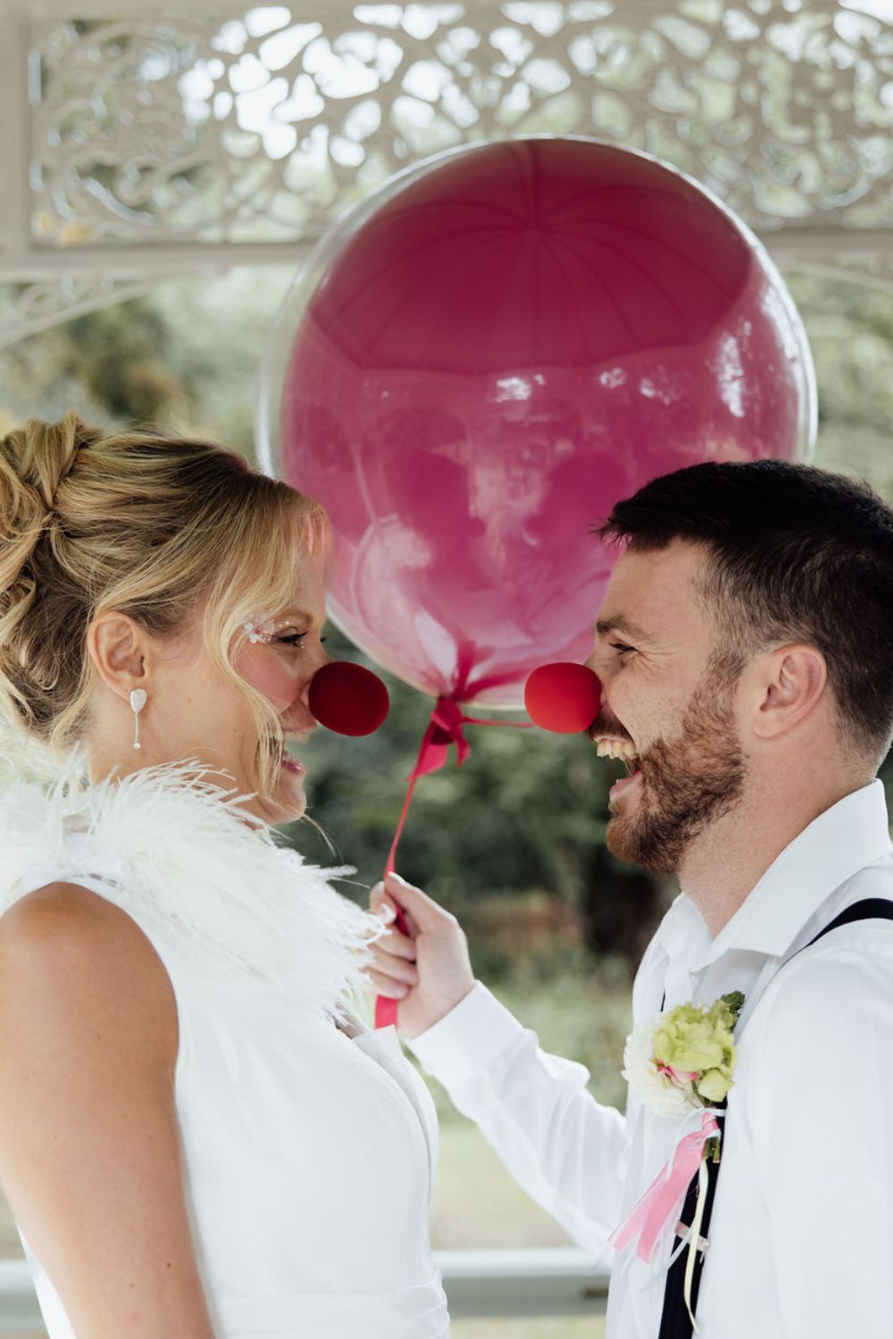 bride and groom wearing red noses holding a red balloon