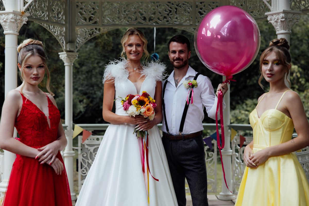 couple stand with their bridesmaids holding large ballon at carnival wedding