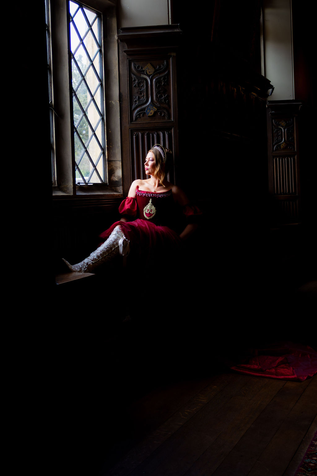atmospheric photo of a bride wearing a red wedding dress in the window of a castle wedding venue