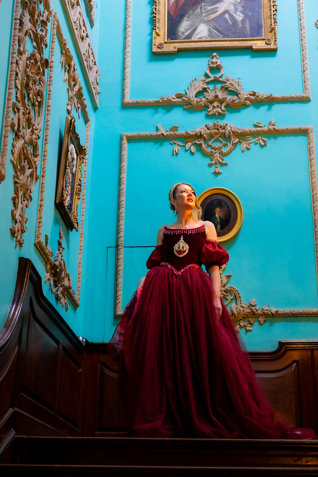 bride wearing red dress stood on the stairs at Powderham Castle - historic wedding venue