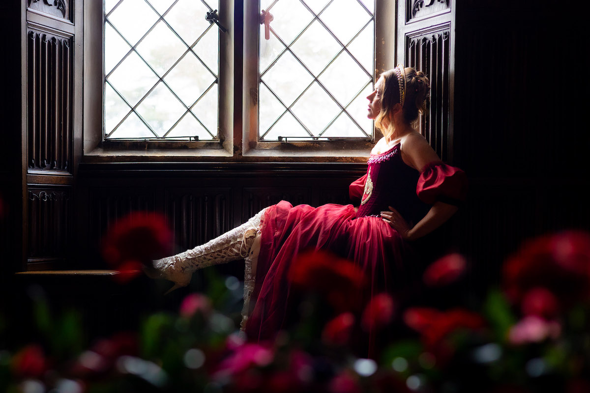 atmospheric photo of light on a bride wearing a red dress surrounded by carved wood walls of a castle