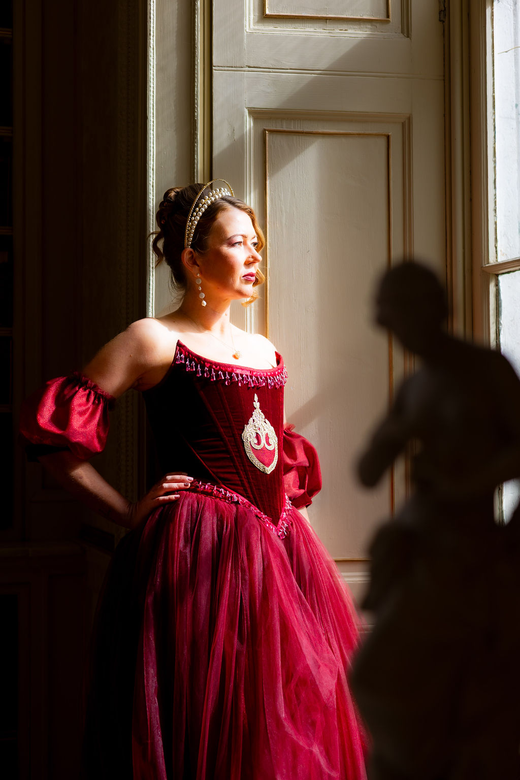 bride wearing a red wedding dress stood at the window of her historic wedding venue