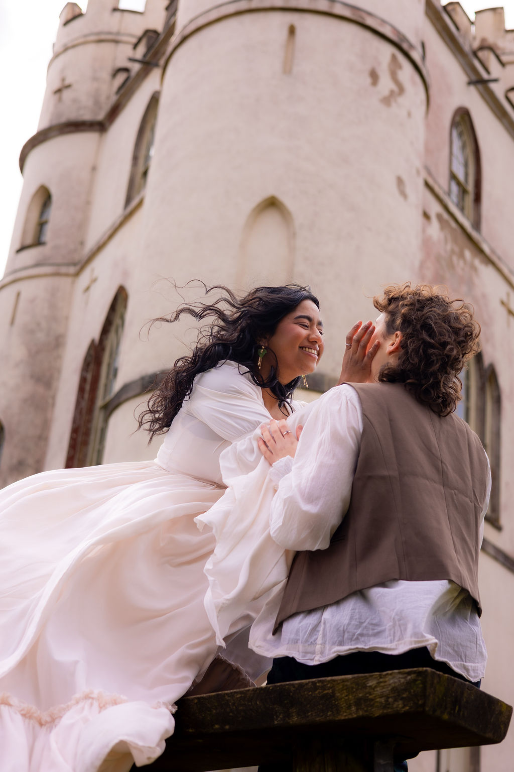couple embracing in the wind outside of historical wedding venue at Pre-Raphaelite inspired wedding