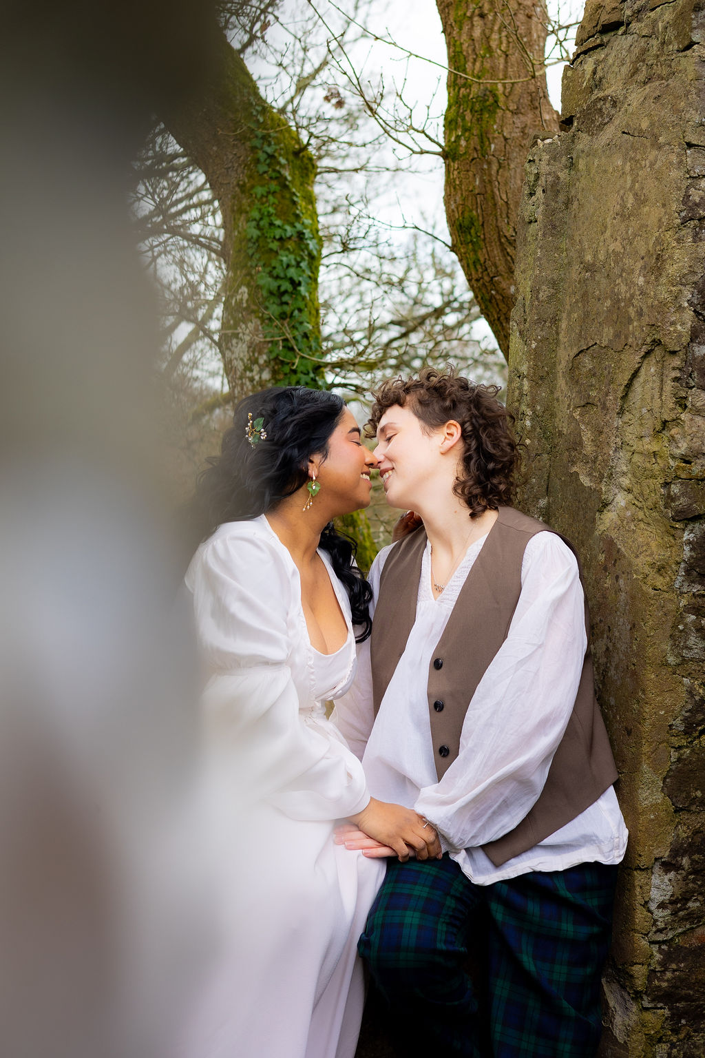 couple sat on an ancient wall holding hands about to kiss as part of Pre-Raphaelite inspired wedding