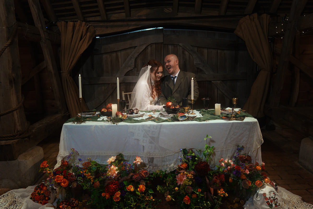 bride and groom sat at their wedding breakfast table which is layered with lace and florals