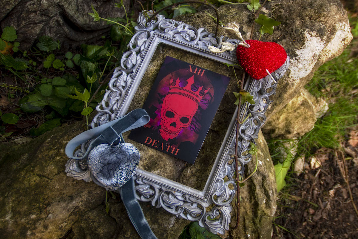 flat lay of 'death' tarot card set in a frame with handmade heart brooch and choker necklace for Wuthering Heights wedding