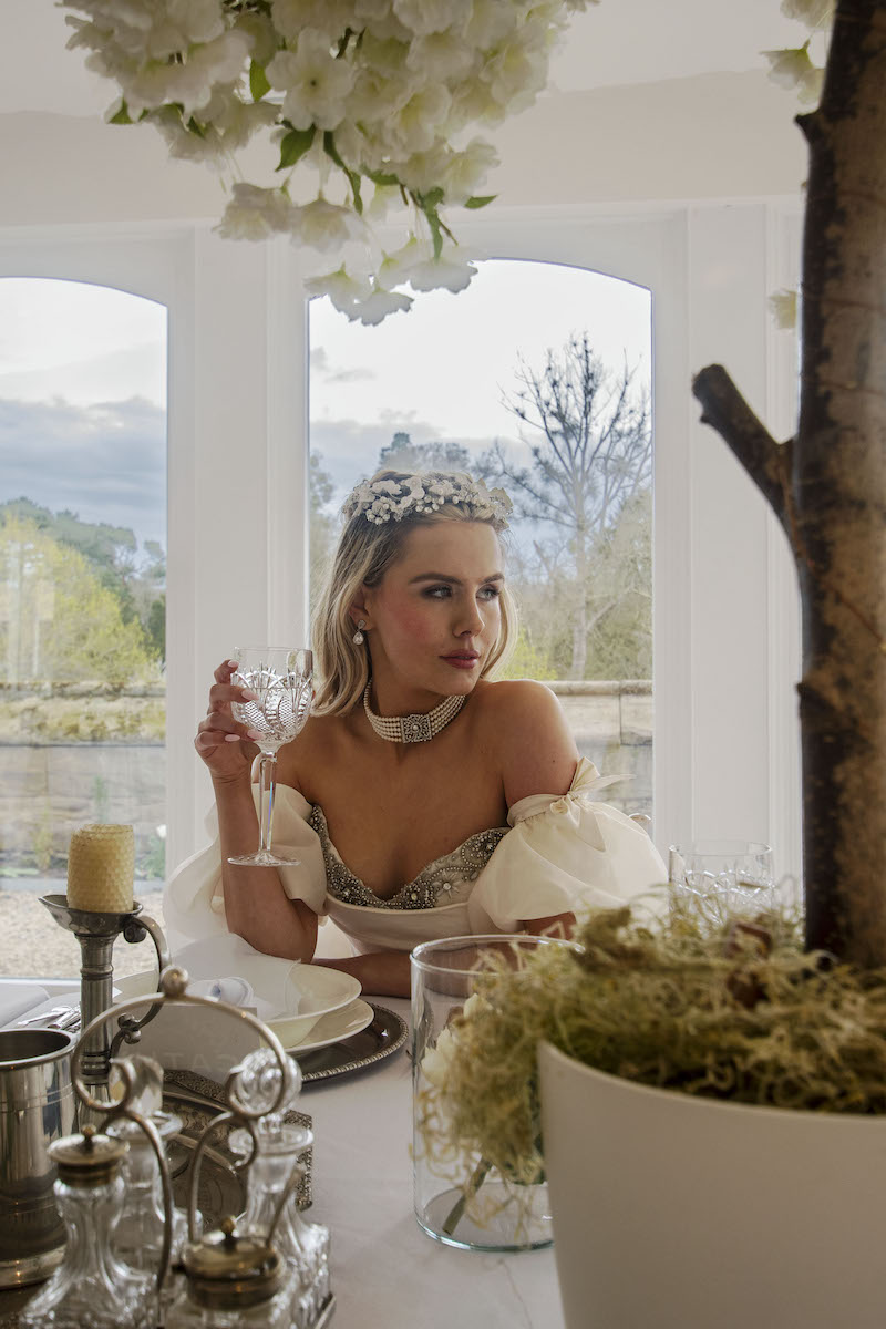 bride sat at the wedding breakfast table with moss and blossom tree framing her