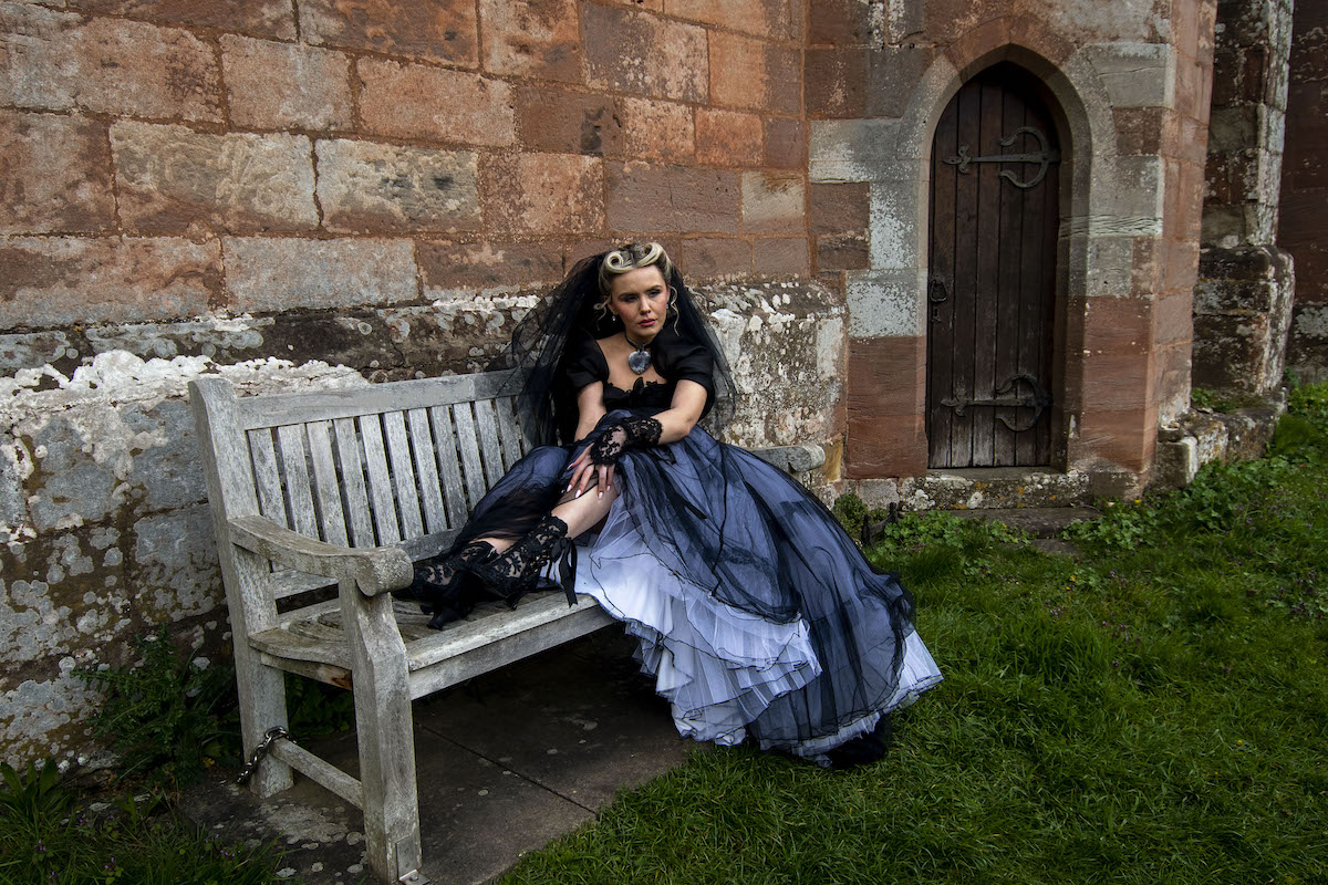 bride wearing black wedding dress and veil sat showing her black lace wedding boots