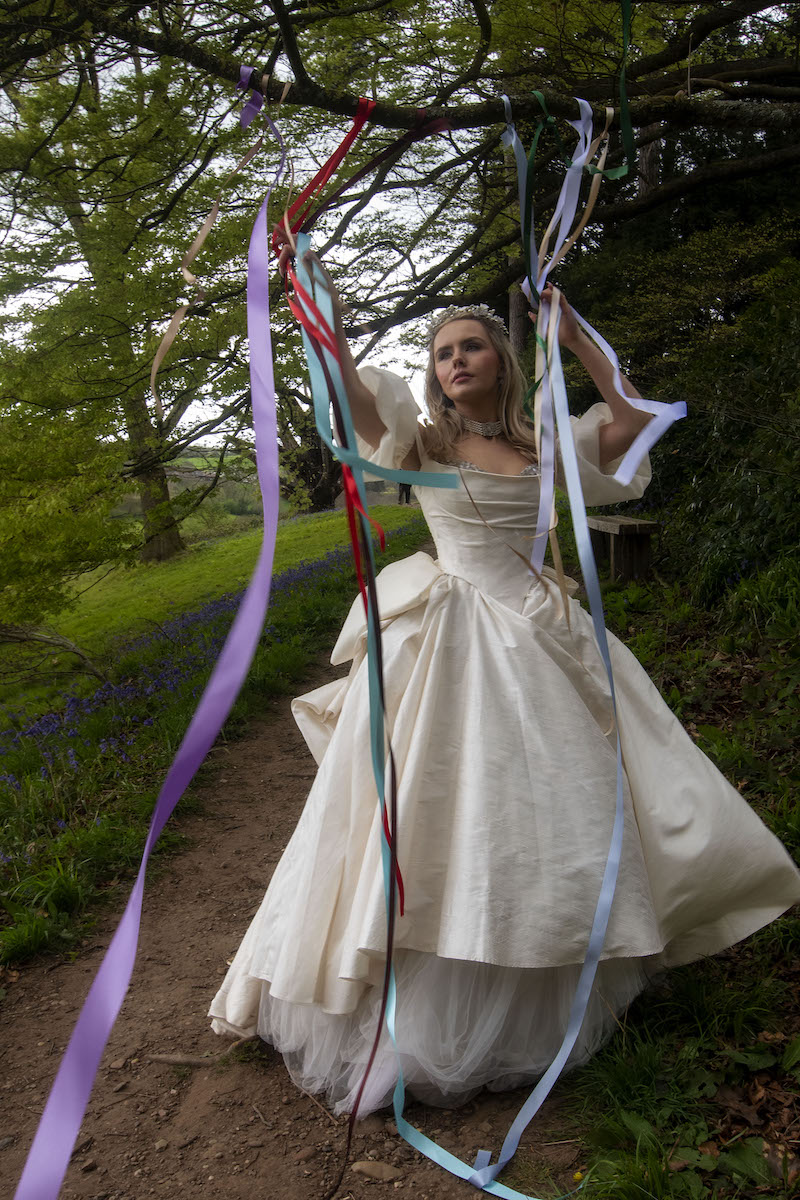 bride wearing ballgown wedding dress stood beneath a tree with ribbons hanging like in Wuthering Heights
