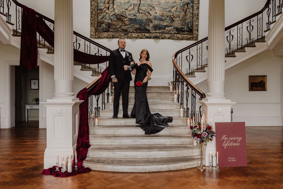 bride and groom stood on the staircase which is dressed with drapes, candles and flowers