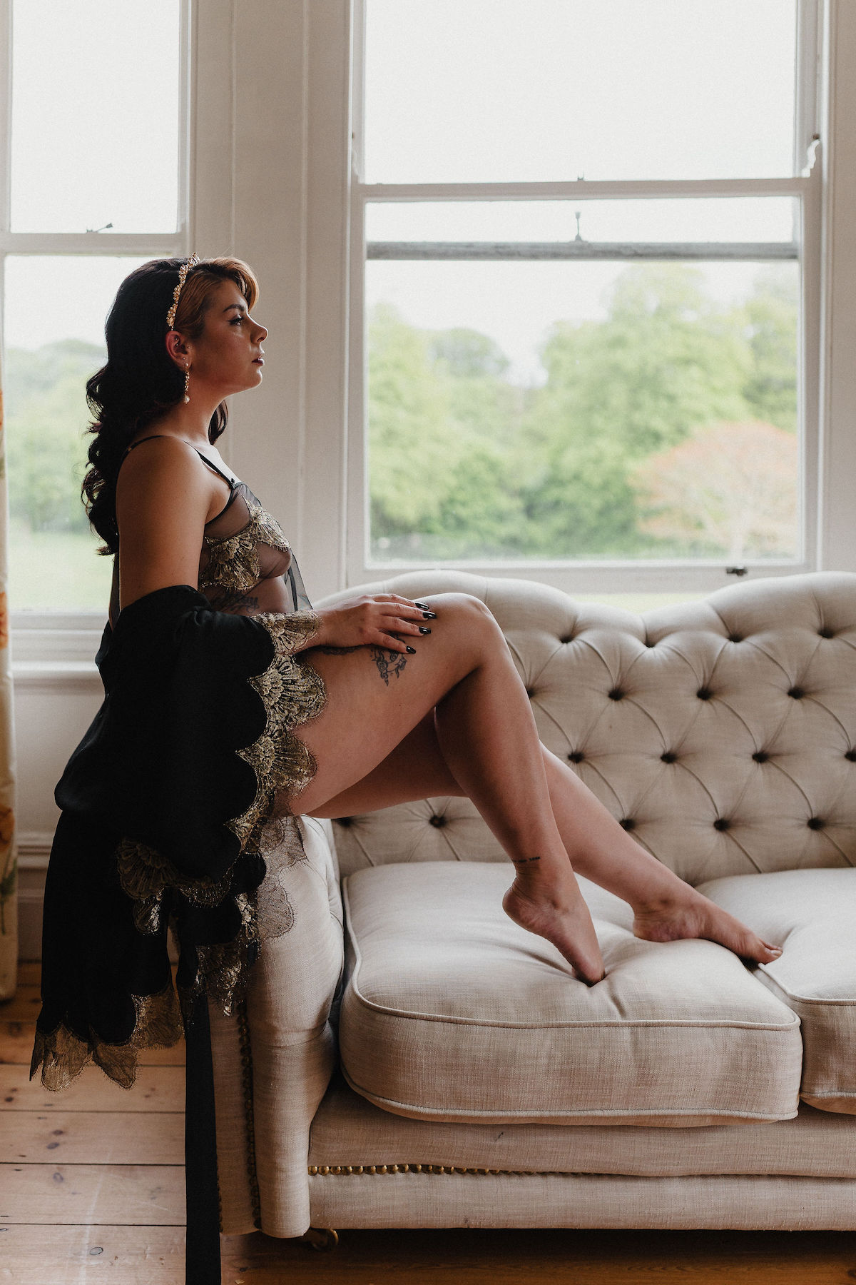 bridal boudoir portrait where the bride sits on the arm of a sofa wearing handmade lingerie and robe