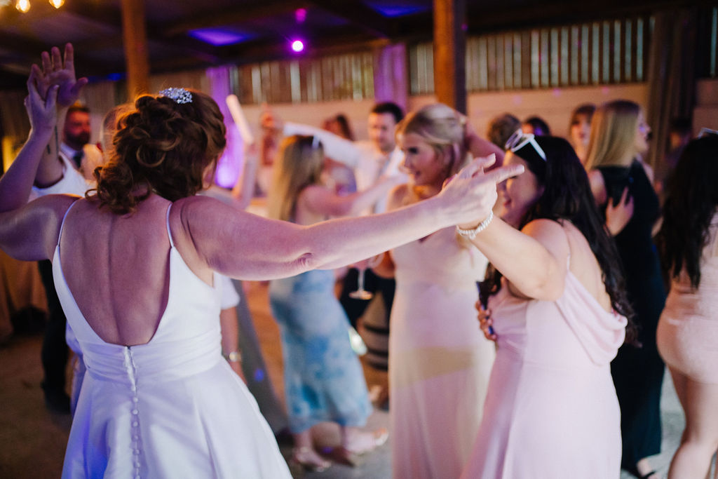 bride dances with her bridesmaids who wear pastel rainbow dresses
