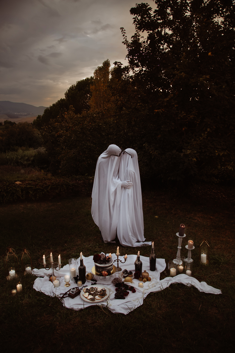 couple dressed as ghosts wearing sunglasses kiss as the sun sets for alternative halloween wedding portrait