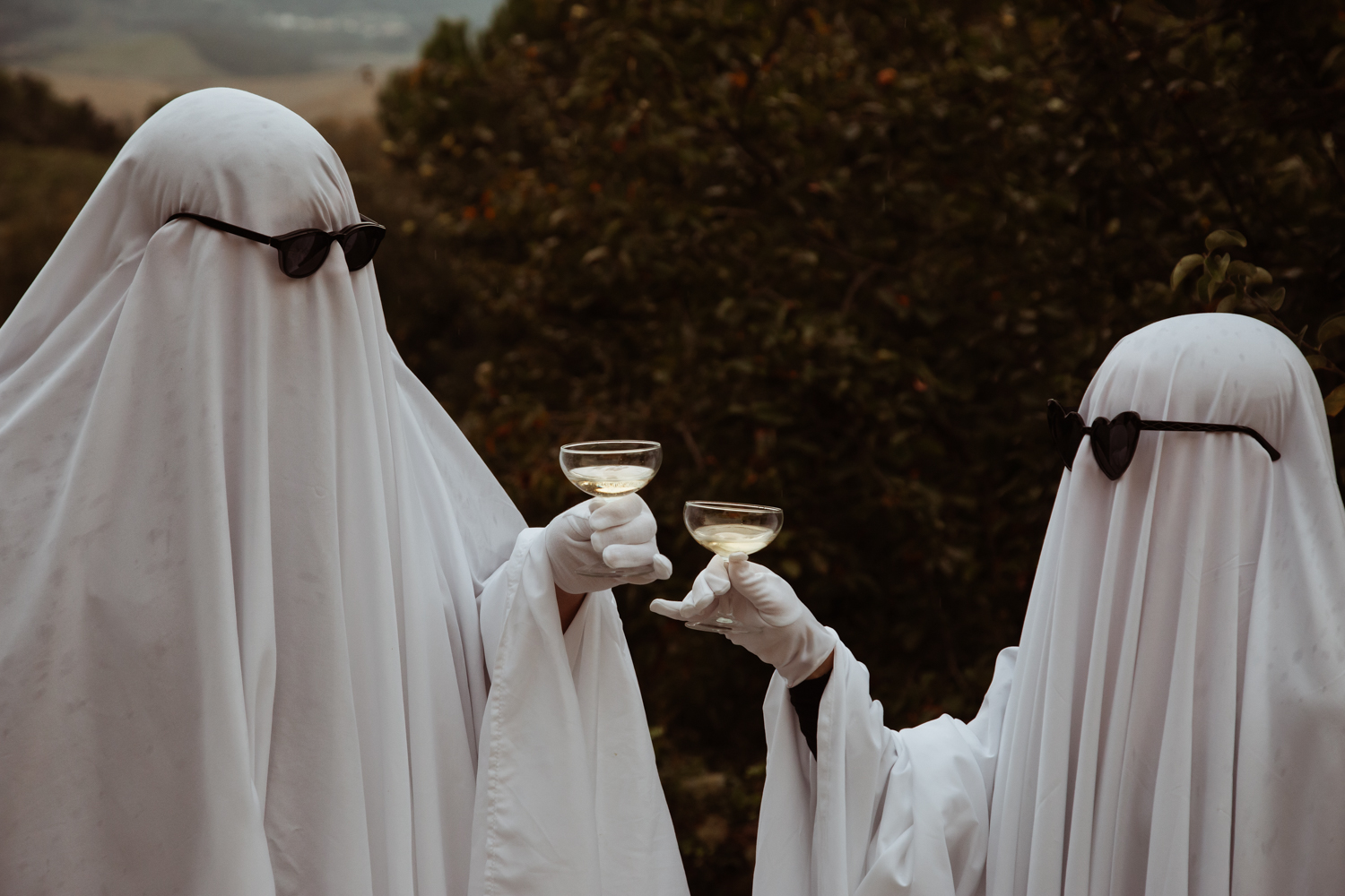 close up of bride and groom dressed as ghosts toasting their halloween wedding with champagne glasses