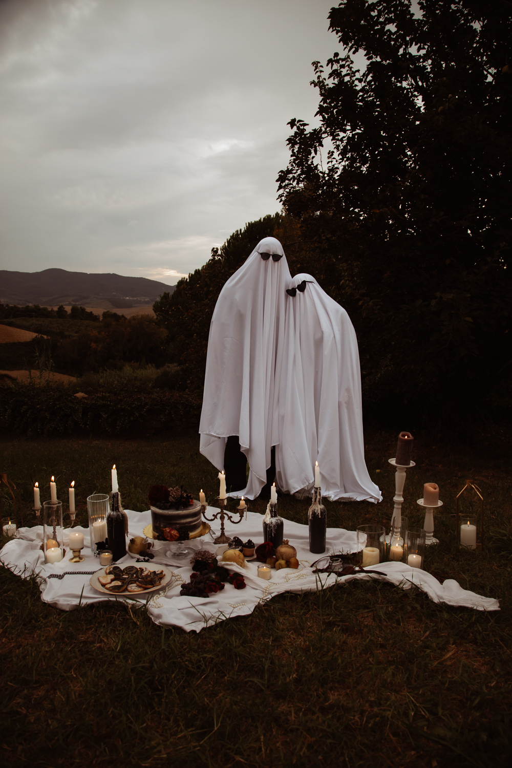 couple dressed as ghosts wearing sunglasses stood in front of their wedding breakfast picnic