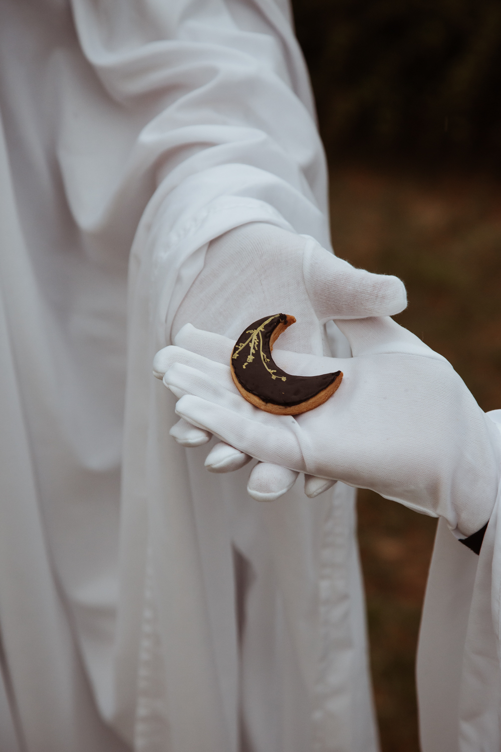 close up of two hands wearing white gloves holding a moon shaped biscuit