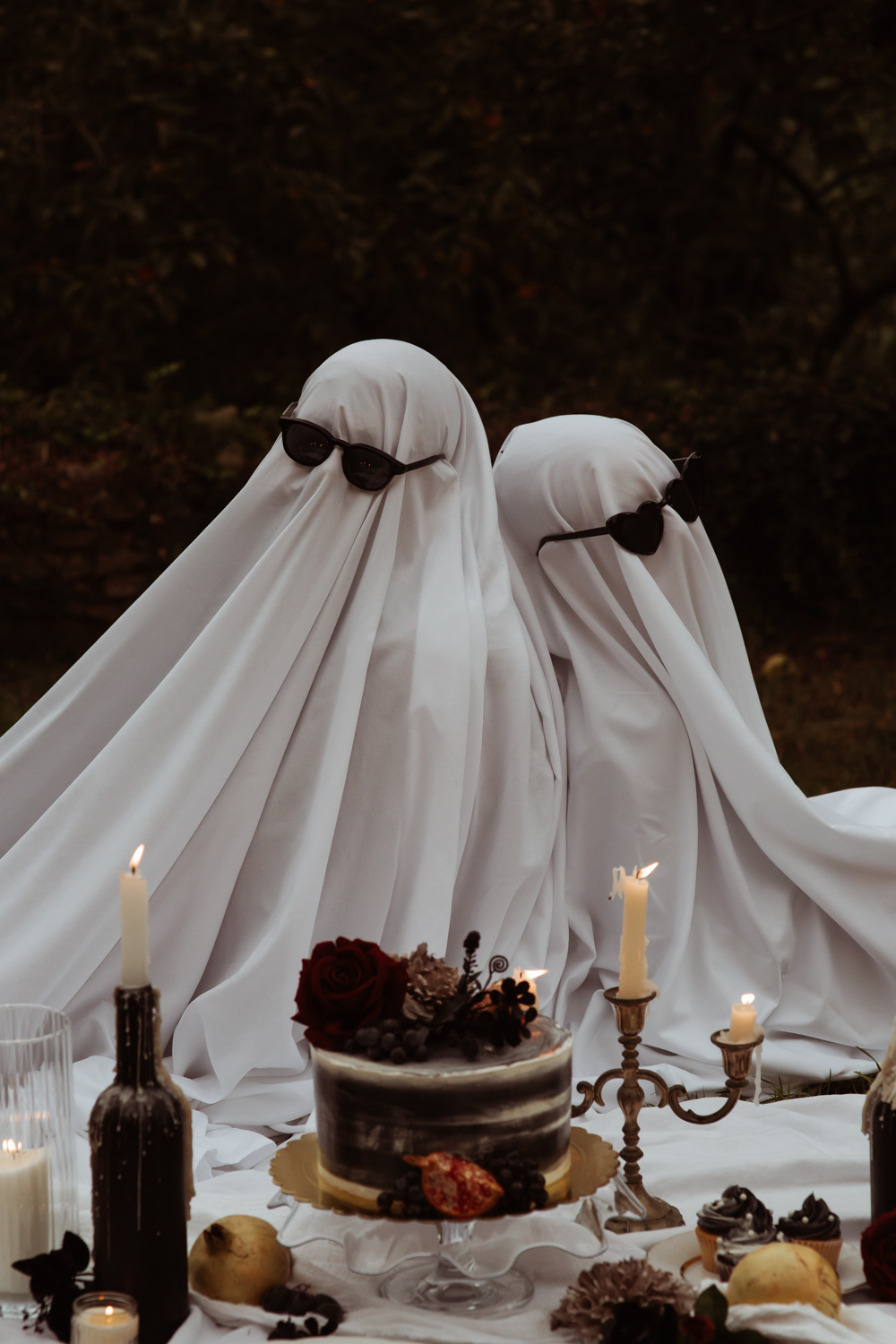 couple dressed as ghosts wearing sunglasses sat back to back for halloween portrait