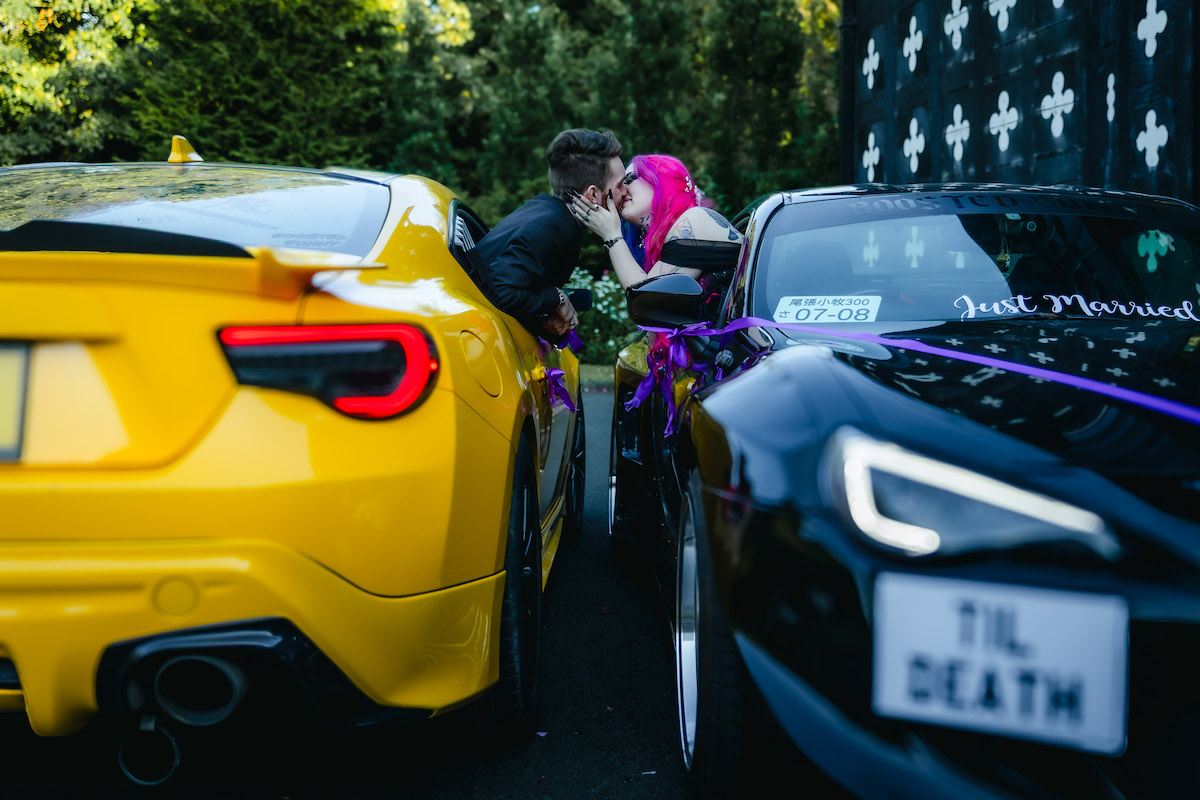 bride and groom leaning out of the windows of their sports cars kissing