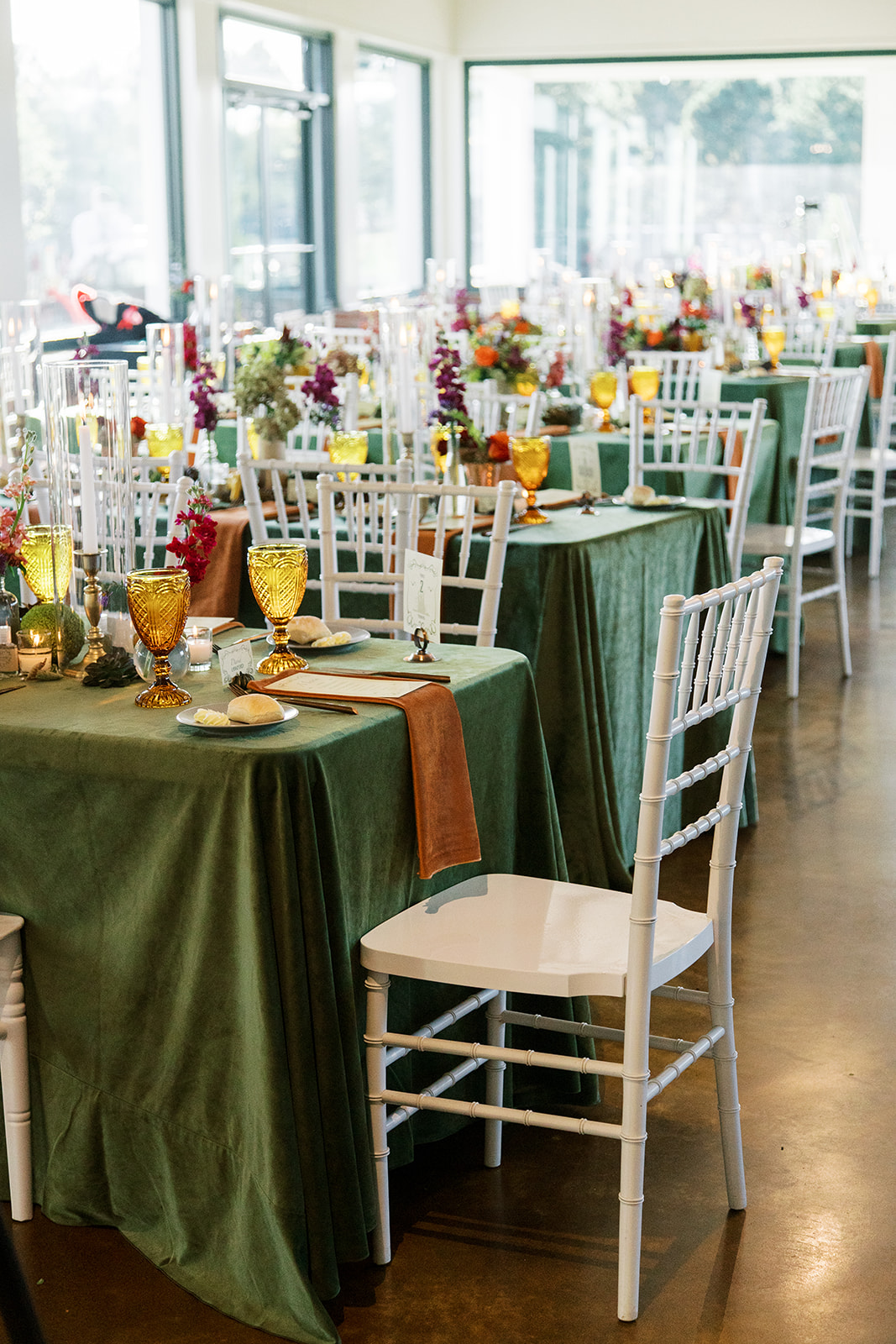 wedding breakfast tables covered in green velvet cloths, amber glasses, gold napkins and autumn toned flowers
