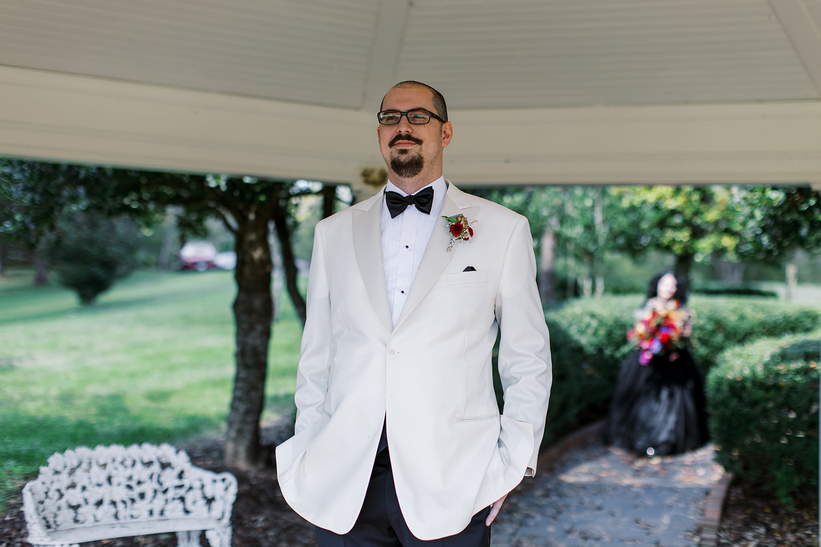 focus in groom in white while his bride is out of focus in the background walking to him for first look