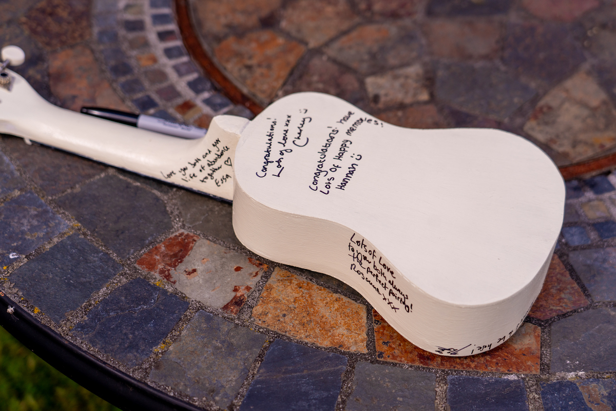 close up of white ukulele used as a wedding guest book with peoples messages of love written on it