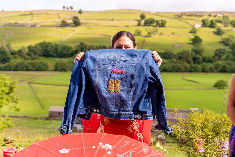 bride holding up her handmade denim jacket embroidered with Just married again on it