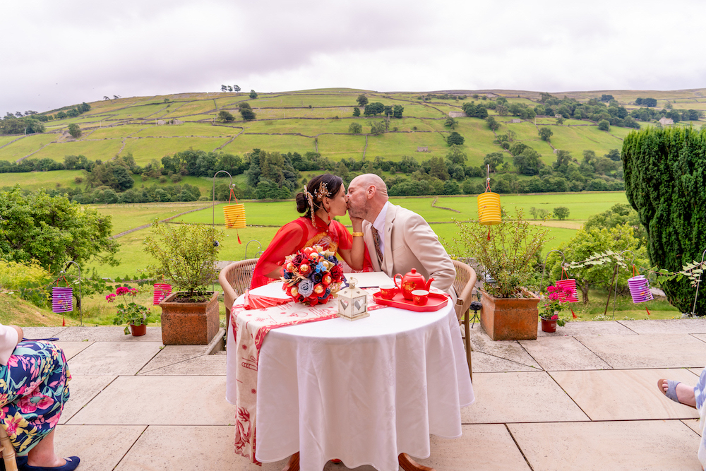 bride and groom kiss at the wedding ceremony table with the Yorkshire hills behind them
